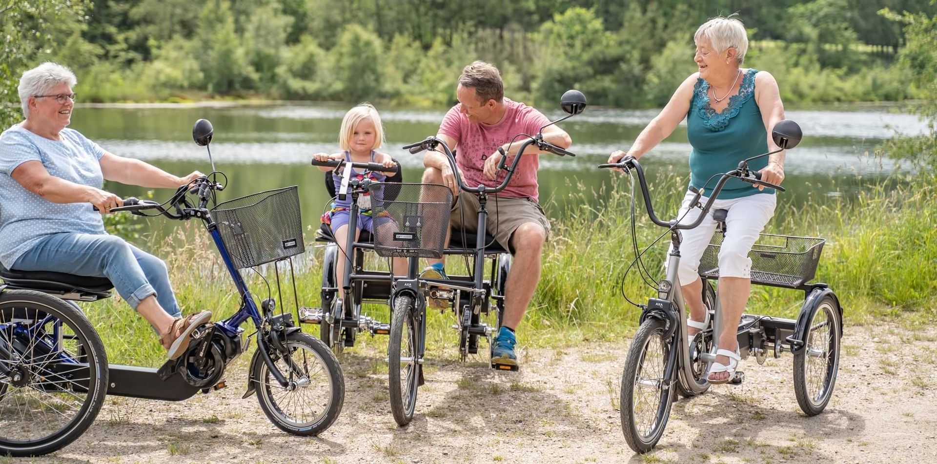 Eine Familie fährt mit Fahrrädern am Ufer eines Sees entlang, umgeben von Bäumen und einer ruhigen Landschaft.