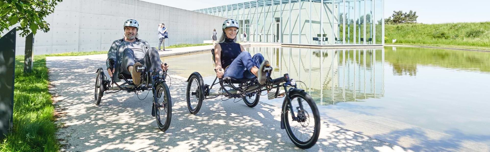 Zwei Personen fahren mit Fahrrädern neben einem Teich.